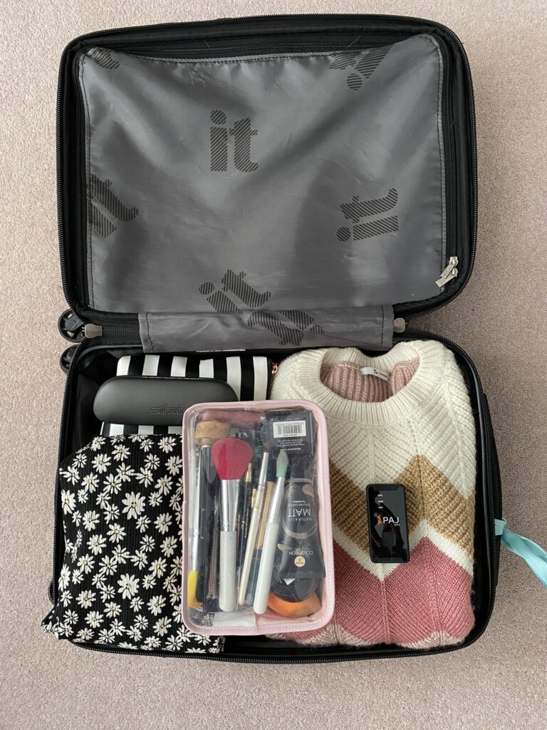 Open suitcase with clothes, makeup, toiletries and the PAJ Easy Finder 4G tracker