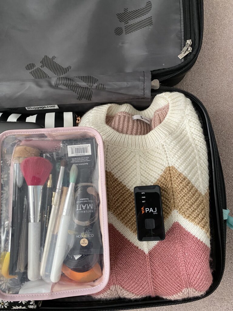 Open suitcase with clothes. cosmetics, clothes and PAJ Easy Finder 4G tracker
